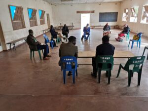 A small group of community leaders sit spaced apart in a large, sparsely furnished hall in Gwanda during COVID-19, holding a socially distanced meeting to discuss grassroots organizing and restoring the people’s movement.