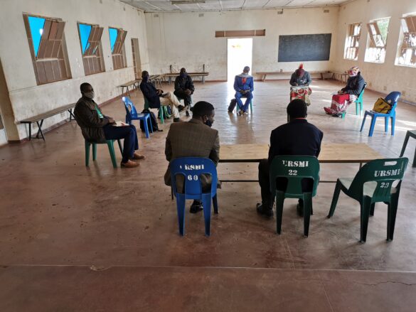 A small group of community leaders sit spaced apart in a large, sparsely furnished hall in Gwanda during COVID-19, holding a socially distanced meeting to discuss grassroots organizing and restoring the people’s movement.